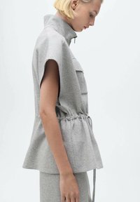 Haut gris clair à manches courtes avec un col haut, taille cintrée et poches latérales. Fabriqué à partir d'un matériau doux et texturé.