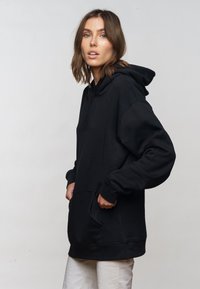 Black hoodie made of soft fabric, featuring a spacious front pocket, long sleeves, and a drawstring hood. Simple and casual design.