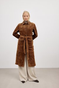 Brun suedeblazer med bælte i taljen, to forlommer og spids krave. Båret over lysebeige bukser med en glat tekstur.