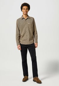 Bruine en blauwe geruite longsleeve shirt met een zak, gecombineerd met zwarte broeken en bruine schoenen; casual pasvorm en knopen ontwerp.