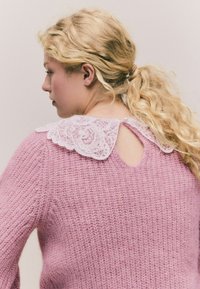 Różowy sweter robiony na drutach z teksturowanym wykończeniem, z białą koronkową kołnierzykiem i małym wycięciem na plecach z zapięciem na guzik.