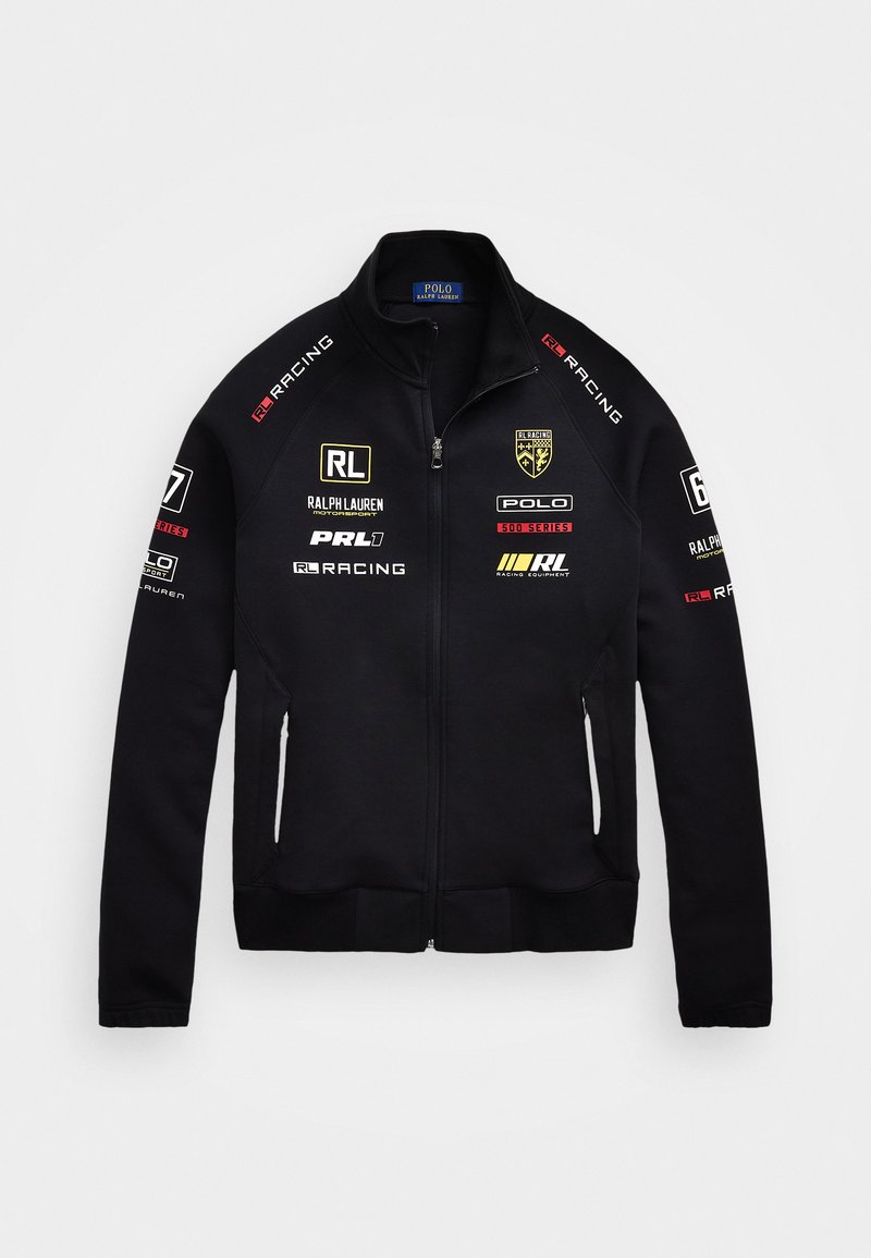 Svart zip-up jakke laget av mykt materiale, med flere logoer i hvit, gull og rød. Inkluderer høy krage og sidelommer.