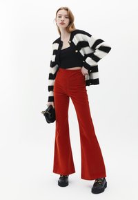 Svart och vit randig stickad cardigan, kort svart topp, röda plyschbyxor med utställda ben och svarta platåskor med guldinslag.