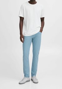 Witte kortomarm t-shirt gecombineerd met lichtblauwe slim-fit broek en grijze sneakers. De stof lijkt soepel met subtiele textuurdetails.