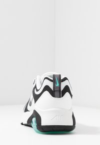 Svart och vit atletisk sko med en texturerad ovandel, teal-accenter och en synlig luftkuddenhet i sulan. Har en randig design.