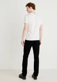 Tricou alb din bumbac, cu mâneci scurte și decolteu rotund, asortat cu pantaloni negri, prezentat din spate pe un fundal alb.