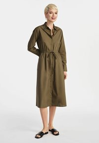Oliwkowa długa sukienka koszulowa z guzikiem z przodu, kołnierzykiem, długimi rękawami i ściągaczem w talii. Połączona z czarnymi klapkami.