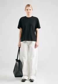 Zwarte korte mouwen t-shirt gecombineerd met brede witte broek. Model houdt een zwarte leren tote bag vast, met een zachte textuur en minimalistisch ontwerp.