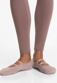 Light pink ballerina-style slippers with dual straps, textured fabric, and a fitted design, paired with form-fitting mauve leggings.