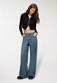 Giacca nera a coste con zip, abbinata a jeans in denim azzurro chiaro a gamba larga e scarpe con piattaforma nere. Design semplice e moderno.