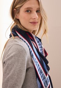 Mehrfarbiger Schal mit einem geometrischen Muster, das marineblau, rot und hellblau Akzente setzt. Aus weichstoff gefertigt, fällt er elegant um den Hals.