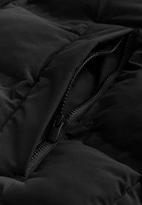 Chaqueta de plumas negra con secciones acolchadas; presenta una cremallera negra a lo largo de la apertura, destacando una textura suave y un diseño duradero.
