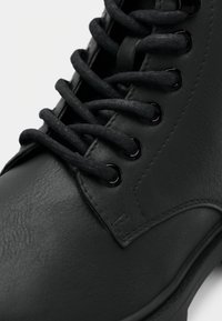 Gros plan sur une botte en cuir noir avec de grosses lacets ronds passés à travers six œillets métalliques sur un côté.