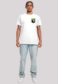 Hvit bomulls t-skjorte med et grafisk lomme-design med en grønn og rød tegneseriefigur. Kombinert med lyseblå denim jeans og hvite sko.