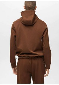 Felpa marrone realizzata in tessuto testurizzato con vita regolabile tramite cordino, presenta un cappuccio e polsini elasticizzati, mostrando un design minimalista e una parte posteriore senza cuciture.