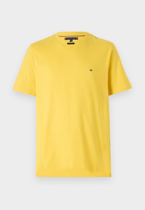 Sárga pamut póló V nyakkivágással, rövid ujjakkal és kis logóval a bal mellen. Zökkenőmentes textúra, hétköznapi dizájn.