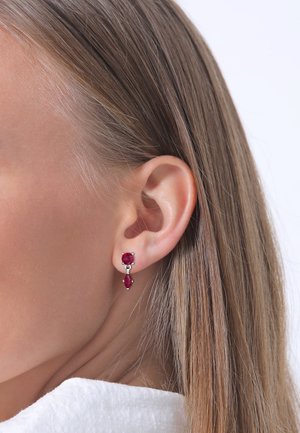 Boucles d'oreilles rouge rubis avec un design à deux pierres, comprenant une pierre ronde et une pierre marquise montées sur un support en métal argenté.