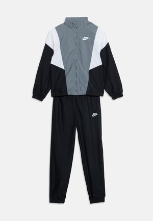 Survêtement deux pièces Nike avec blocs de couleur gris, blanc et noir, comprenant une veste zippée et des poignets élastiques, logos Nike sur la veste et le pantalon.