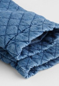 Geknaagd blauw stoffen rol met een gestructureerde afwerking, voorzien van een ruitpatroon en zichtbare stiksels. Zacht, lichtgewicht en flexibel materiaal.
