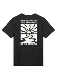 Schwarzes Baumwoll-T-Shirt mit einem weißen Grafikmotiv von Sonnenaufgang und Fluss. Der Text beinhaltet "WENN DU DIE SONNE NICHT FINDEN KANNST" und "SEI DIE SONNE."