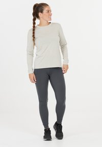Lichtgrijze langslavende shirt met ronde hals, gecombineerd met donkergrijze leggings en zwarte sportschoenen, op een effen achtergrond.