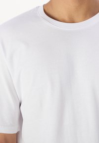 Witte katoenen t-shirt met een ronde halslijn en korte mouwen. Glad oppervlak, minimalistisch ontwerp en geen zichtbare graphics of patronen.