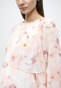 Φλοράλ φόρεμα σε απαλό ροζ σιφόν με στρογγυλή λαιμόκοψη, μακριά μανίκια και ζώνη που δένει στη μέση σε ίδιο χρώμα. Διακριτικά σχέδια και υφές.