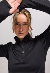 Zwart, langarm sporttop met een hoge kraag en een halve rits, met een gladde textuur en een subtiele logo op de borst.