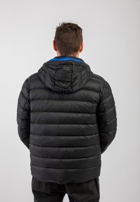 Zwarte pufferjack met een capuchon, voorzien van doorgestikte gedeelten en een blauwe voering die zichtbaar is bij de kraag. Zachte, gladde textuur.