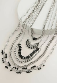 Slojeviti srebrni lanci s crnim detaljima, koji sadrže različite karike, teksture i stilove, uključujući perlate i geometrijske uzorke.