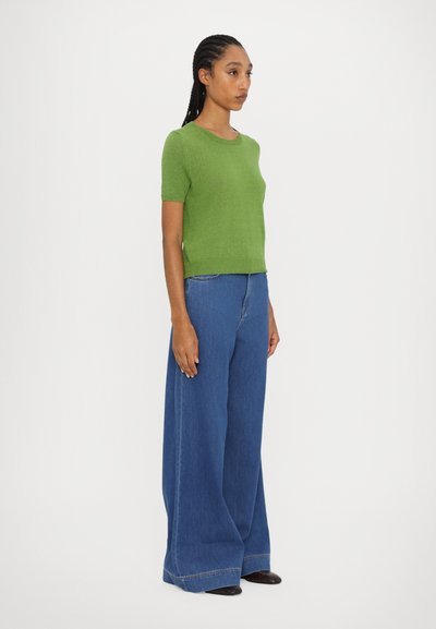 Grøn kortærmet sweater lavet af blødt strikket materiale, parret med brede blå denimjeans med en frynset kant og synlig syning.