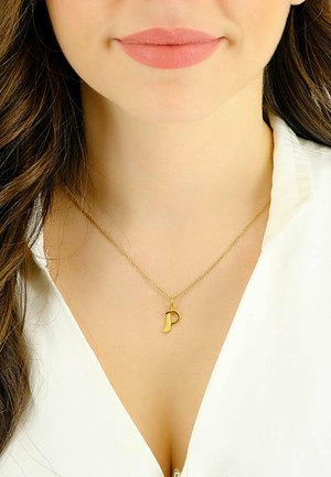 Collana d'oro con un piccolo ciondolo a forma di lettera "P", con una catena delicata e un design semplice e liscio, indossata su una maglia bianca.