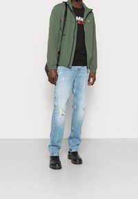 Grön lättviktsjacka, svart t-shirt, slitna ljusblå jeans och svarta ankelstövlar. Har en axelväska med mönstrad design.