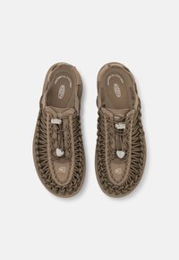 Brown slip-on shoes with woven cord design, featuring an anatomical footbed and a textured surface. Minimalist branding on the insole.