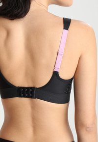 Svart bh med justerbare rosa stropper, krokfeste og teksturert detaljering bak. Laget av glatt stoff med en strukturert design.