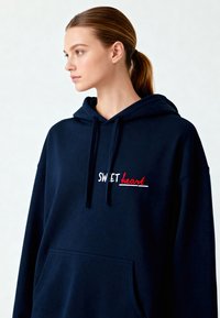 Sweatshirt à capuche bleu marine en tissu doux avec l'inscription "SWEET heart" en broderie blanche et rouge, doté d'une poche avant et de cordons de serrage ajustables.