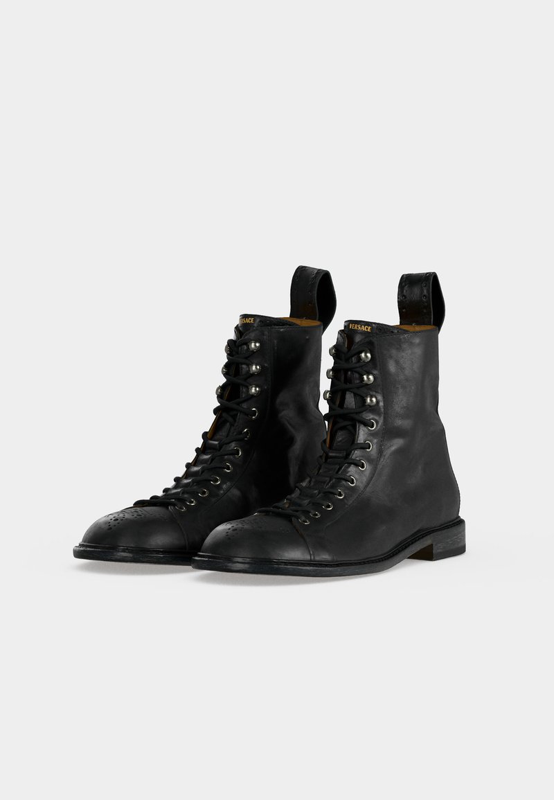 Schwarze Leder-Schnürstiefeletten mit Zuglaschen, Metallösen und dezentem Branding auf der Zunge, nebeneinander auf einem einfarbigen Hintergrund platziert.
