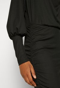 Gros plan sur la main d'une personne reposant à côté d'une robe noire à manches longues froncées avec des manches bouffantes.