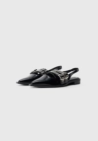 Mustat, kärjellään terävät slingback-latkat, joissa on kaksinkertaiset solkipannat, hopeiset niitit ja matalat pinottu korot.