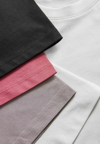 Vier T-Shirts übereinander gestapelt. Die Farben sind schwarz, weiß, pink und hellgrau. Baumwollstoff mit sichtbaren Nähten und glatter Textur.