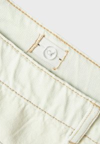 Svijetlozeleni denimski materijal s vidljivom teksturom, s kontrastnim bež šavovima i bijelim dugmetom na pojasu s oznakom.