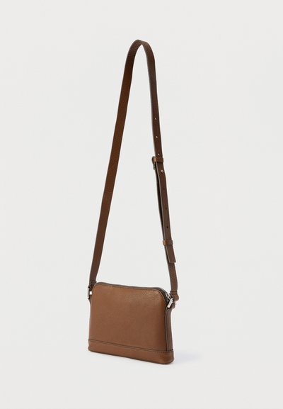 Καφέ δερμάτινη τσάντα χιαστί με ρυθμιζόμενο λουρί και ασημένιο φερμουάρ σε απλό λευκό φόντο.
