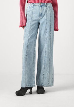 Lyseblå vide jeans med fremtrædende sidesømme, knaplukning og høj talje. Sammen med sorte strukturerede højhælede sko.