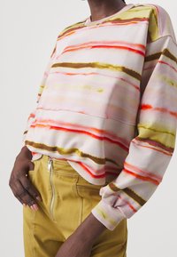 Sudadera colorida con rayas horizontales en rosa, naranja y verde. Cuenta con un escote redondo y un ajuste holgado, confeccionada con un material suave.