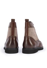 Botas Chelsea de cuero marrón con paneles de tela en patrón espiga, textura suave y detalles de brogue en la parte superior, con una lengüeta de tirón.