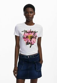 Witte katoenen t-shirt met kleurrijke bloemenprint en de tekst "Vandaag is een goede dag." Gecombineerd met een donkerdenim rok met zakken.