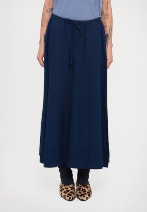 Σκούρο μπλε, μακρύ μάξι φούστα με κορδόνι στη μέση; συνδυασμένη με χοντρές, σκούρες κάλτσες και παπούτσια με λεοπάρ σχέδιο. Λείο, μαλακό ύφασμα.