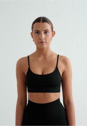 Schwarzer nahtloser Bralette mit dünnen verstellbaren Trägern. Glatte Textur, minimalistisches Design, kombiniert mit hochgeschnittenen schwarzen Unterteilen.