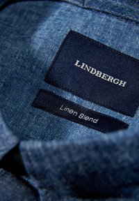 De kraag van het linnenmix shirt heeft een gestructureerde blauwe stof. Labels vermelden "LINDBERGH" in het wit en "Linnenmix" in kleinere letters.