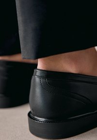 Czarne skórzane buty o gładkiej fakturze i subtelnych detalach w postaci przeszyć, z umiarkowanym obcasem i zaokrąglonym noskiem.